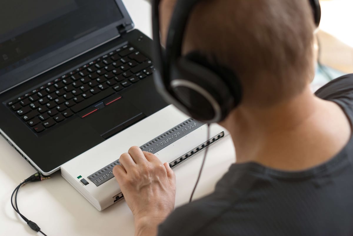 Pessoa com fones de ouvido utilizando um laptop com teclado em Braille.